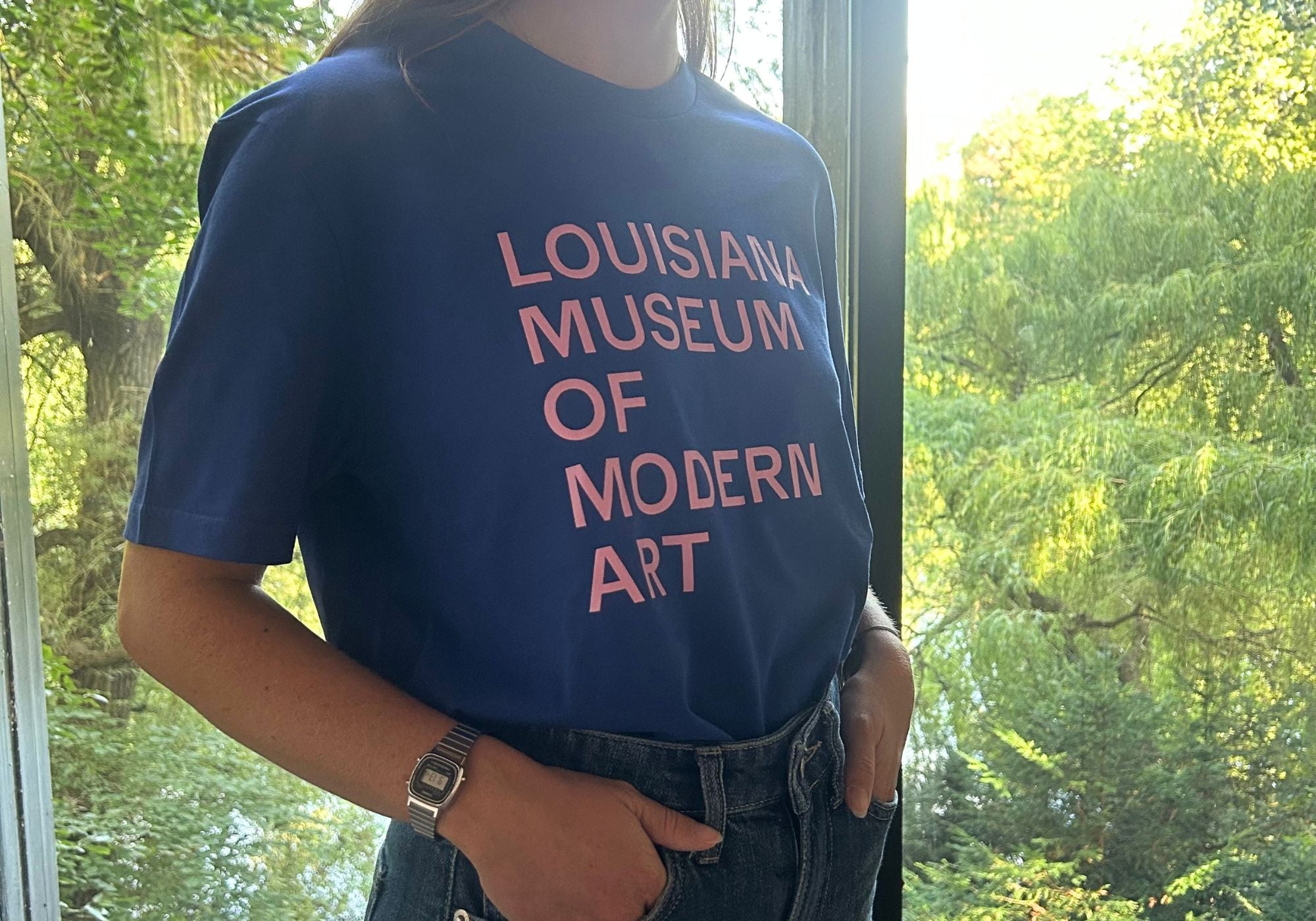 Louisiana T-shirt i blå med teksten “Louisiana Museum of Modern Art” i lyserødt print stylet i Louisianas interiør.
