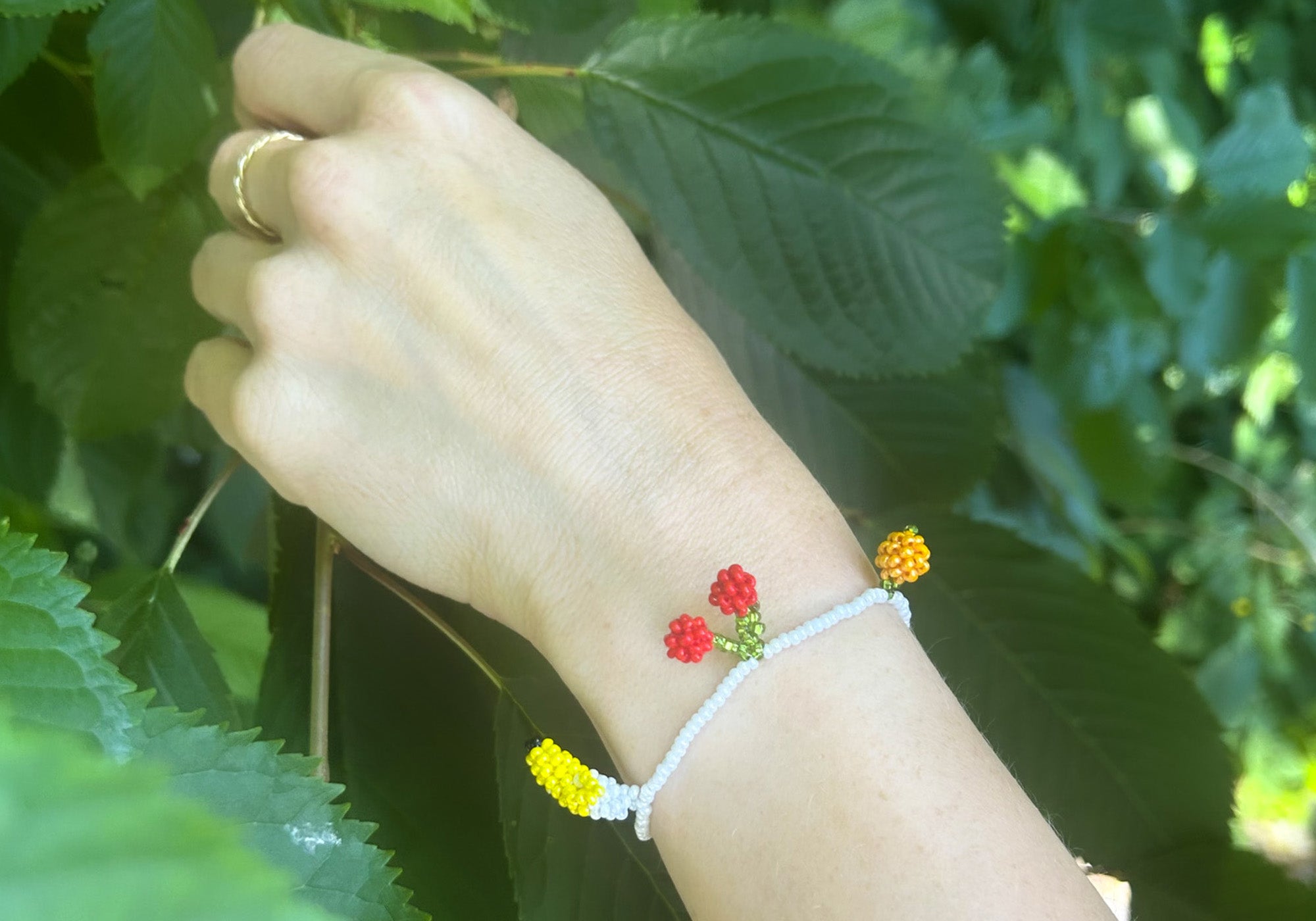 Hvidt armbånd med frugt vedhæng håndlavet i glasperler. to røde jordbær, en appelsin, et kirsebær og en banan. Stylet i Louisianas interiør. Pura Utz