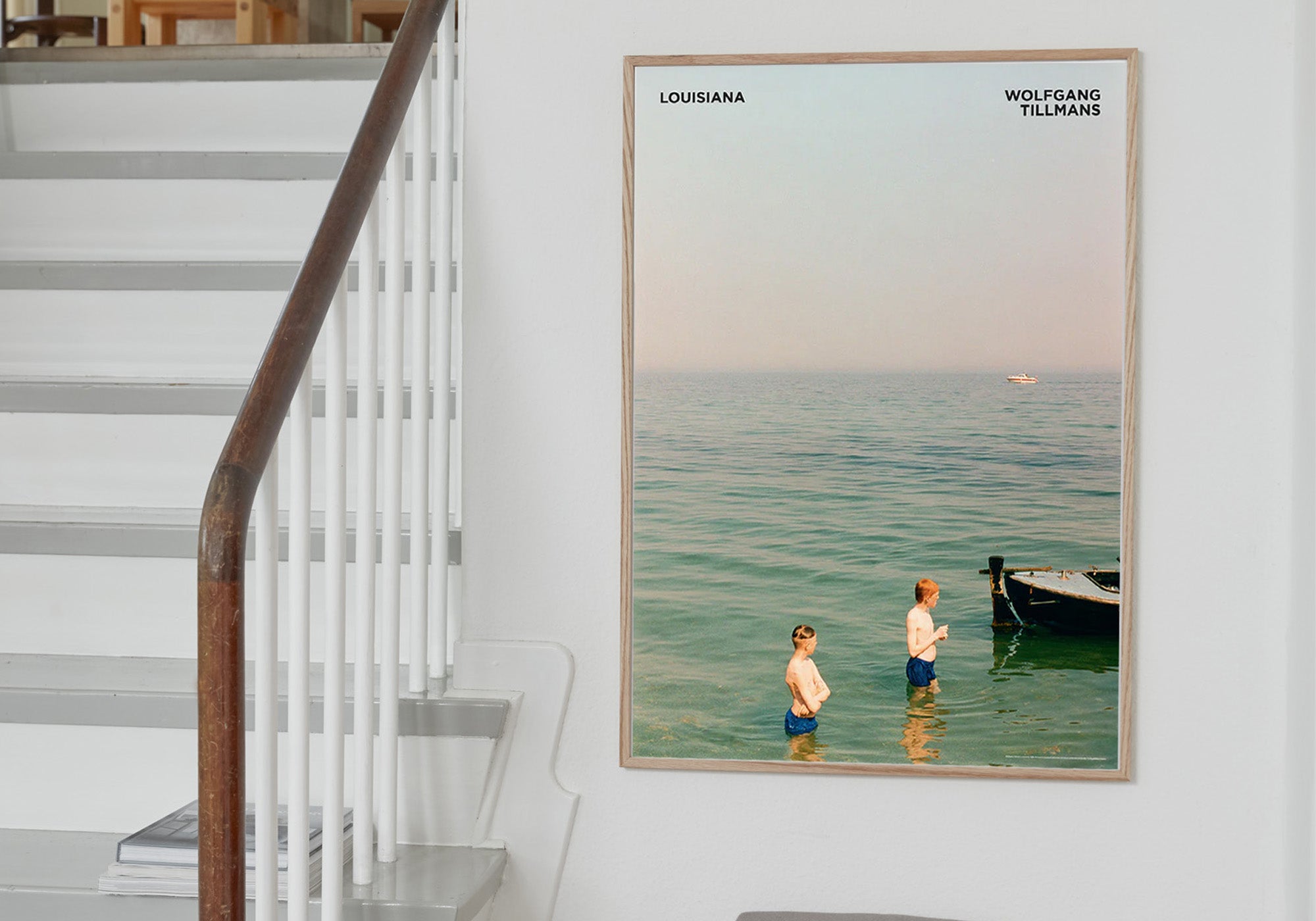 Kunstplakat i refleksfri indramning med Wolfgang Tillmanns værk Louisianas - med to badende drenge i Øresund. Stylet i ramme på væg. Louisiana Museum of Modern Art.