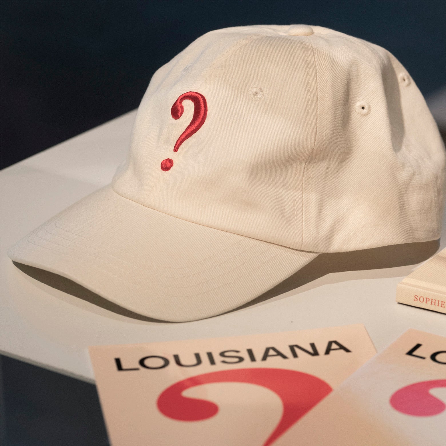 Kasket i bomuld med rødt spørgsmålstegn udgivet i forbindelse med udstillingen Something Missing? med den franske kunstner Sophie Calle i marts 2026. Stylet i Louisianas interiør. Louisiana Museum of Modern Art